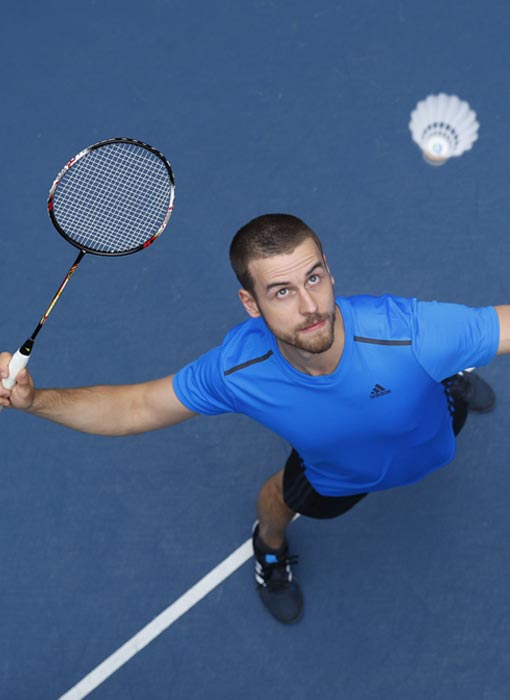 Homme qui joue au badminton et qui porte un t-shirt Adidas bleu
